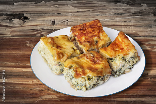 Plate of Freshly baked Serbian Traditional Zeljanica Spinach-cheese Pie slices, set on very old, weathered, cracked, scratched, peeled off, Wooden Table surface. photo