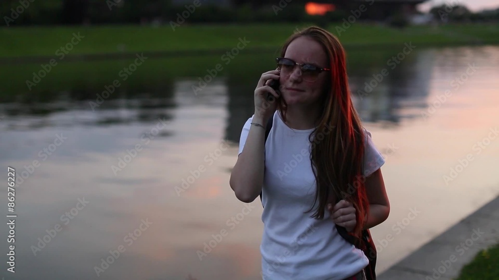 Teenage cute girl talking on mobile phone outdoors evening during sunset. The river embankment. (HD) Teenage cute girl talking on mobile phone outdoors evening during sunset. The river embankment. (HD)