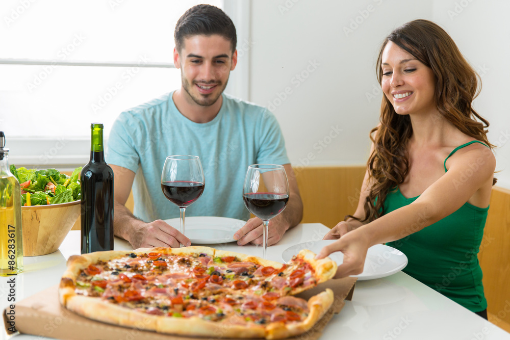 Boyfriend and girlfriend eating a large supreme pizza at home on a date with wine