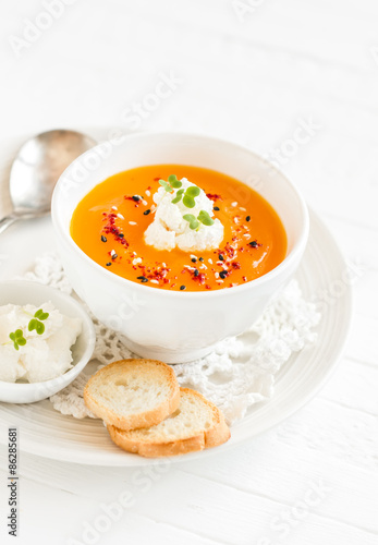 pumpkin soup with cream and paprika in a white bowl on a light wooden background