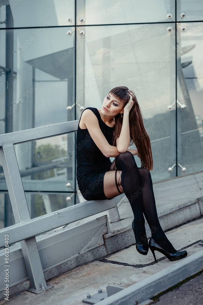 Fashion outdoor portrait of sexy beautiful woman with brown hair wearing in  black dress, hose and high heels. Posing on creative urban background. foto  de Stock | Adobe Stock