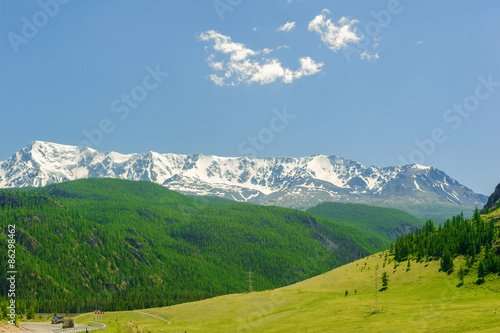 High mountains covered with snow and green forest in Altai in summer