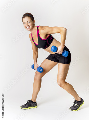 Full length photo of a beautiful, smiling fitness woman lifting weights during a workout. Indoor on a white background © Brocreative