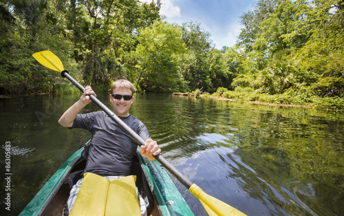 Smiling, happy man kayaking along a beautiful jungle river. Lots of copy space in an active outdoor lifestyle photo