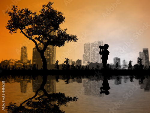 Silhouettes baby boy with camera shooting tree over blurred City
