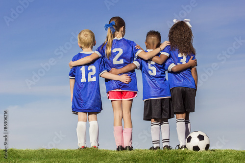Diverse group of boys and girls soccer players standing together with a ball against a simple blue sky background