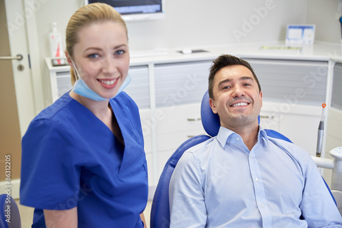 happy female dentist with man patient at clinic