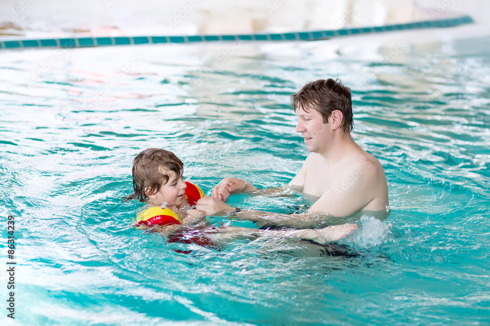 Little kid boy and his father swimming in an indoor pool