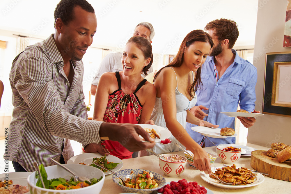 Friends serving themselves food and talking at dinner party