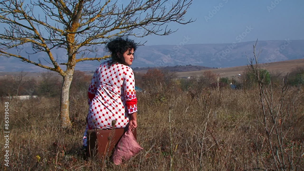 Young Woman In White Dotted Dress Sitting On Suitcase At Nature Young Woman In White Dotted Dress Sitting On Suitcase At Nature