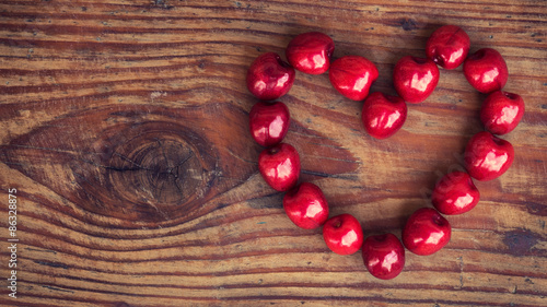 Ripe organic homegrown cherries on wooden background in heart shape photo
