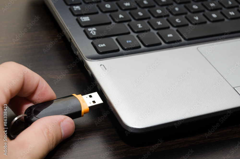 hand with usb flash drive inserting it into laptop computer closeup