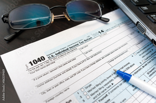 Filling Individual tax return form 1040 on a table with glasses, pen and laptop