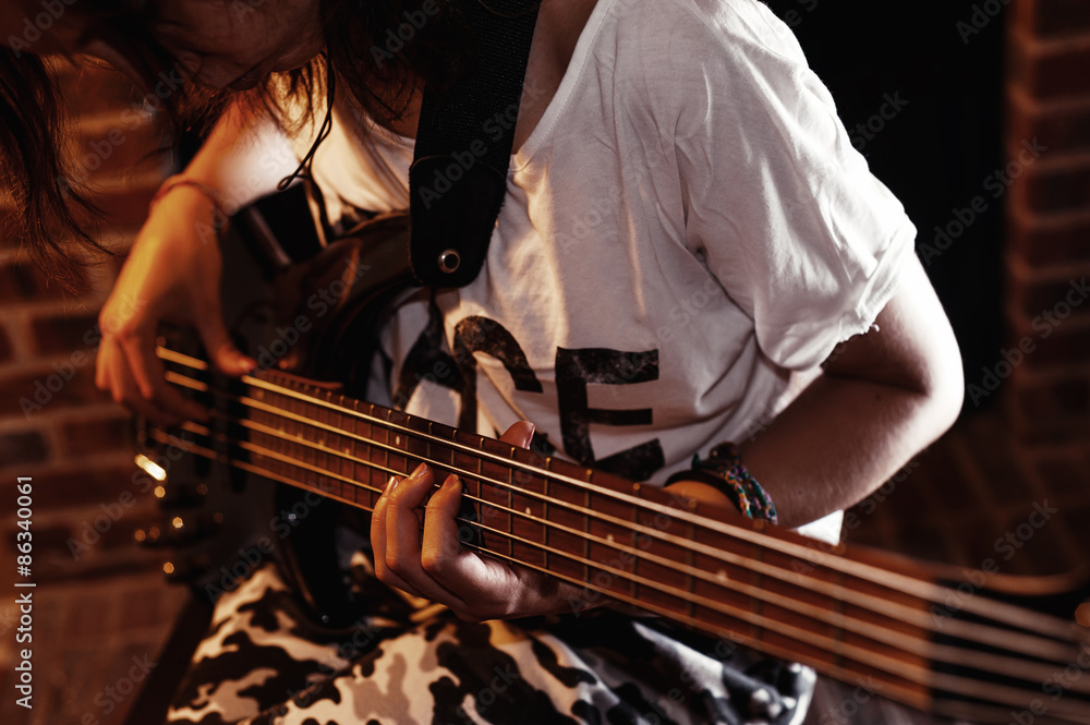 Fototapeta premium Young adult girl playing five string bass guitar. Color image