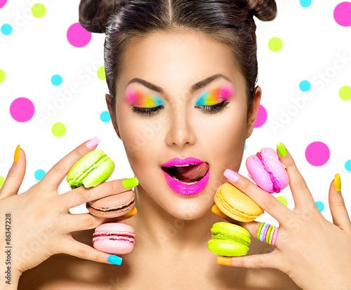 Foto Beauty fashion model girl with colourful makeup taking colorful macaroons