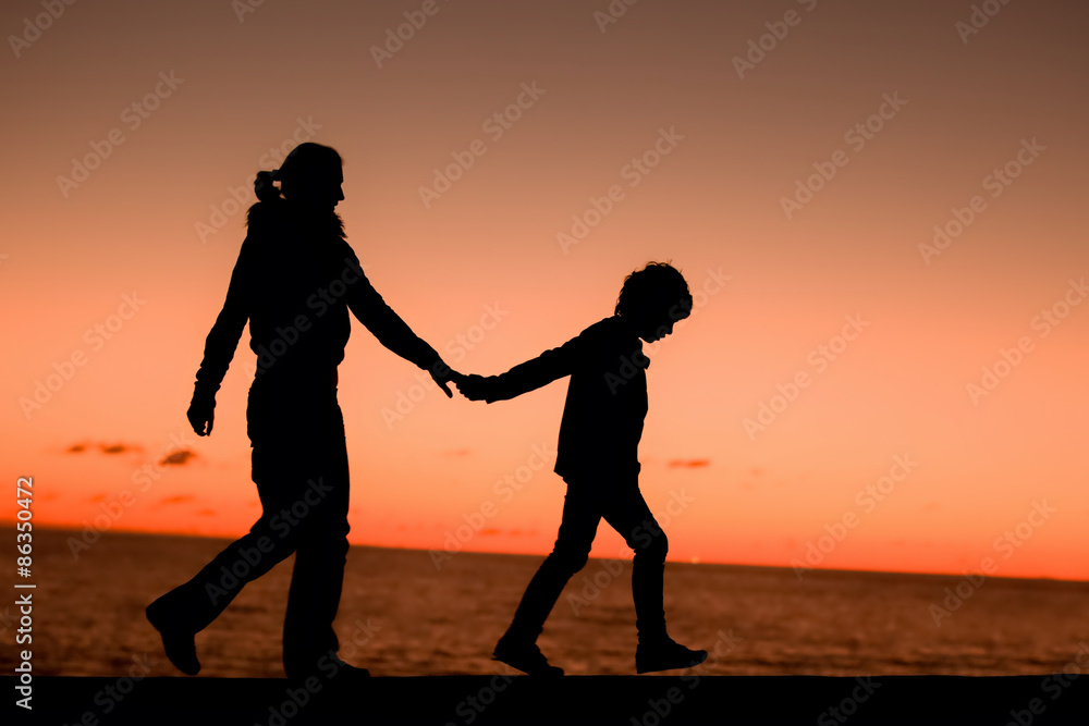 Silhouette of a young mother and her son walking along a pier in