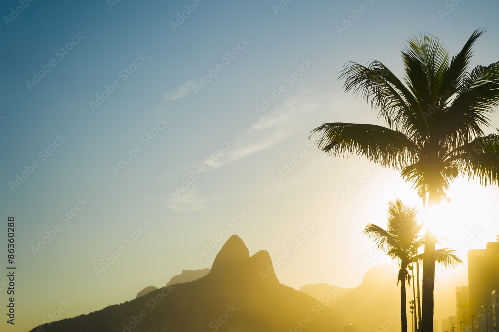 Sunset in Rio de Janeiro Ipanema Beach Brazil with Two Brothers Dois Irmaos Mountain and golden sun through palm trees silhouettes