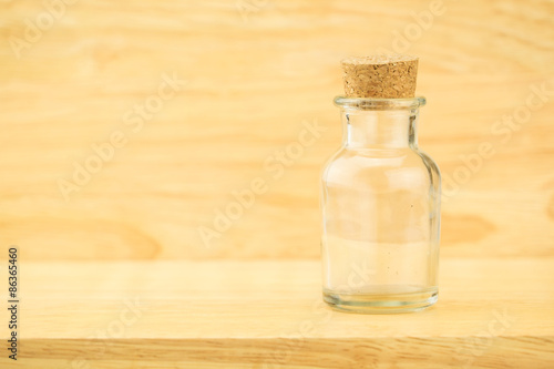 Glass bottle with cork on wood table and blur wooden wall, Copy