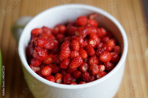 Red fresh wild strawberry in a big white mug stand on a table