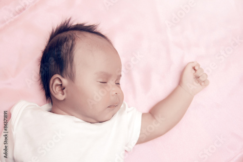 Peaceful baby lying on a bed while sleeping in a bright room