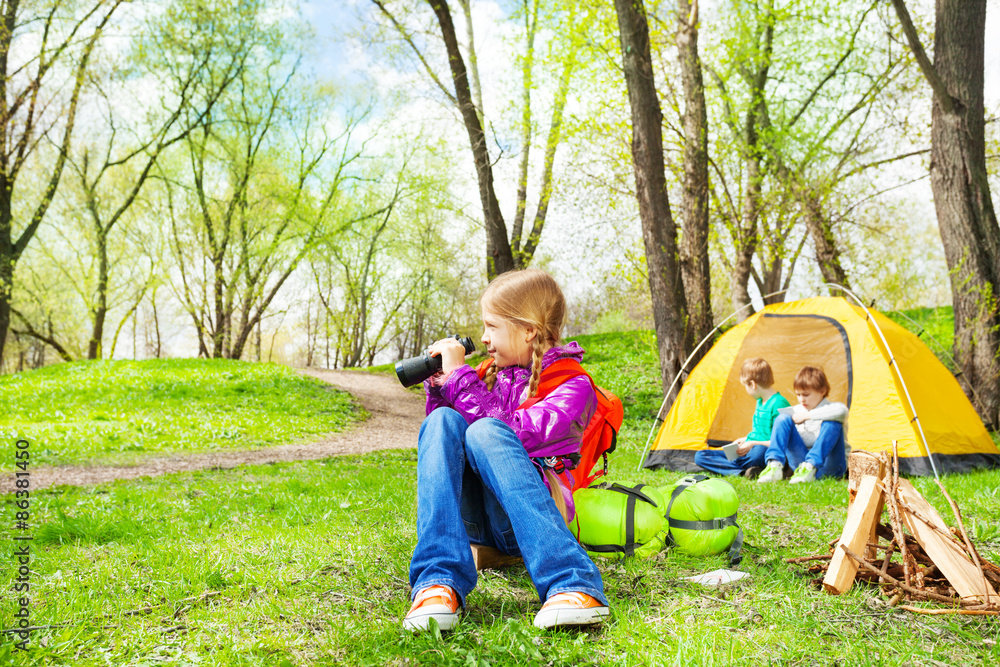 Obraz premium Happy girl with red backpack holds binocular