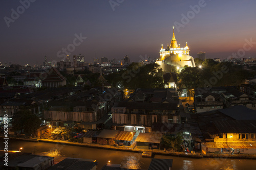 sunset view of phukhao thong, wat saket of Bangkok Thailand. The golden pagoda brightly yellowish among darkest scene of surround building with cloudless sunset sky in background 