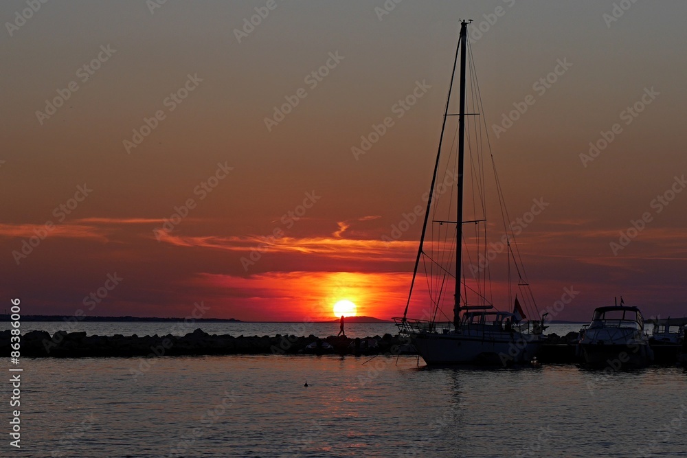 Sunset with yacht, molo and figure in sun in Croatia, Vrsi Mulo beach