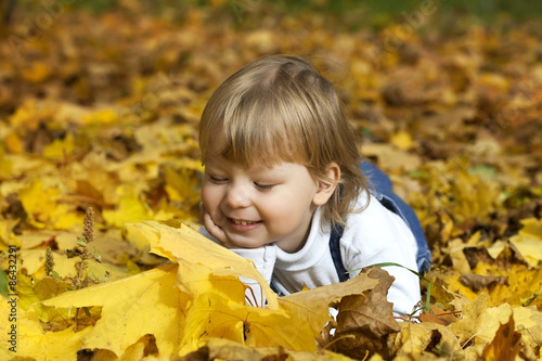 happy boy in leaves of autumn lies