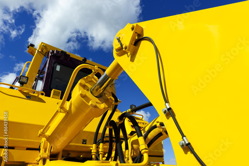 Bulldozer, huge yellow powerful construction machinery with big bucket, focused on hydraulic piston arm, blue sky and white clouds on background  photo