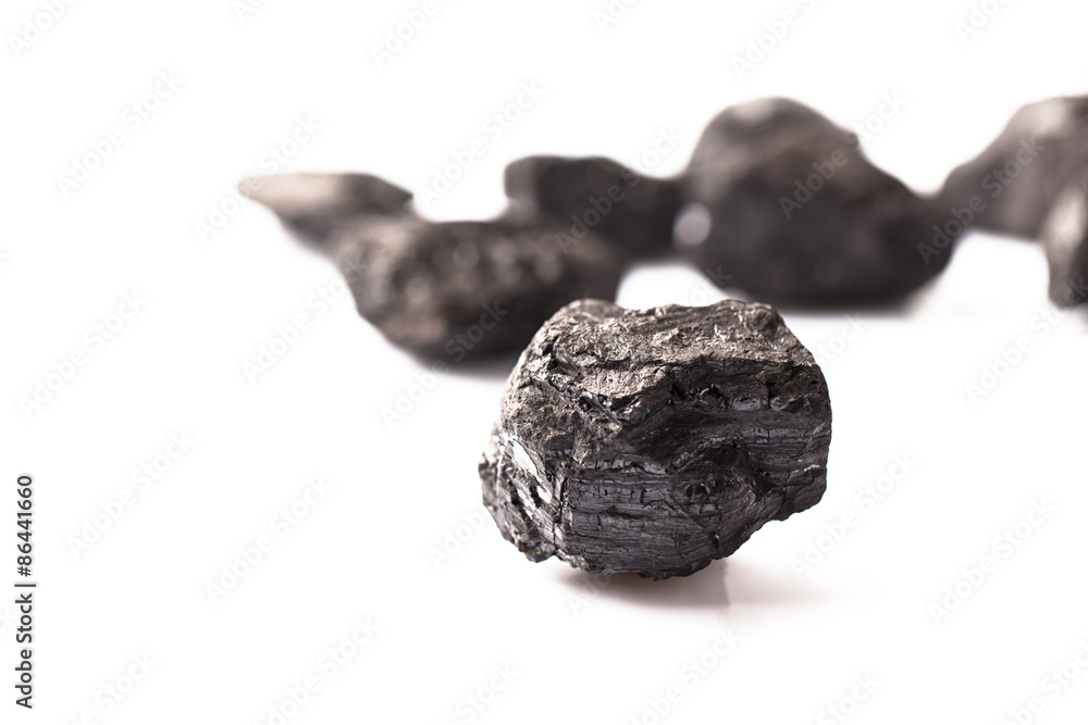 A lump of black coal in focus with some other blurred coal on white background A lump of black coal in focus with some other blurred coal on white background