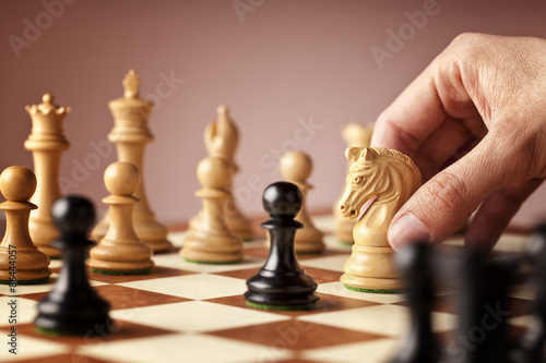 Male hand moving the white chess knight in the middle of a chess game attacking the blacks
