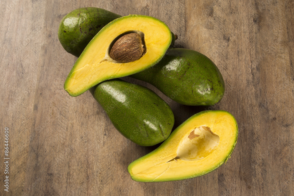 Two whole avocados and a avocado cut in a half over a white surf Two whole avocados and a avocado cut in a half over a white surf