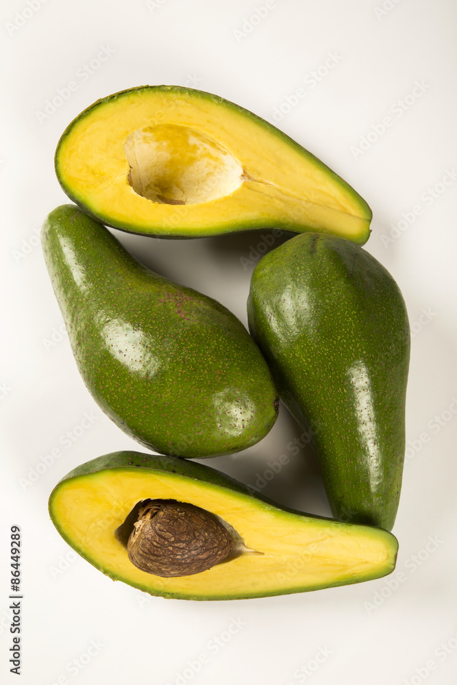Two whole avocados and a avocado cut in a half over a white surf Two whole avocados and a avocado cut in a half over a white surf
