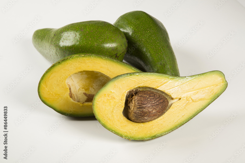 Two whole avocados and a avocado cut in a half over a white surf Two whole avocados and a avocado cut in a half over a white surf
