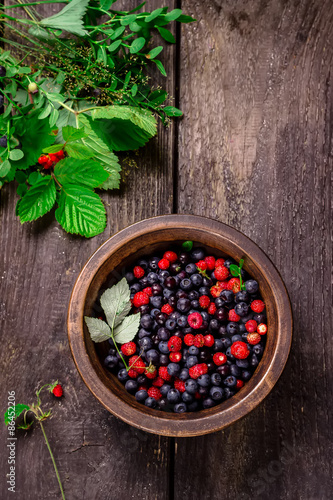 Wooden bowl with wild berries on dark wooden table.