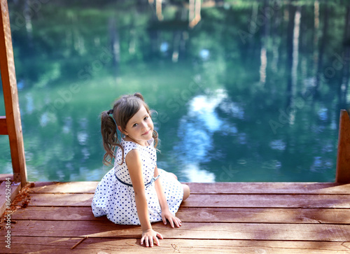 Smiling girl turned around sitting on the bridge by the pond