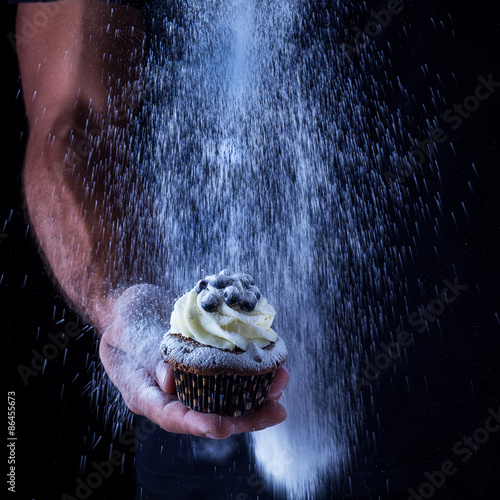 Canvastavla Cupcake in mans hand and the pouring icing sugar