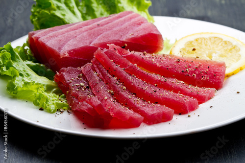 Slices of raw bluefin tuna sashimi on white dish on wood backgr