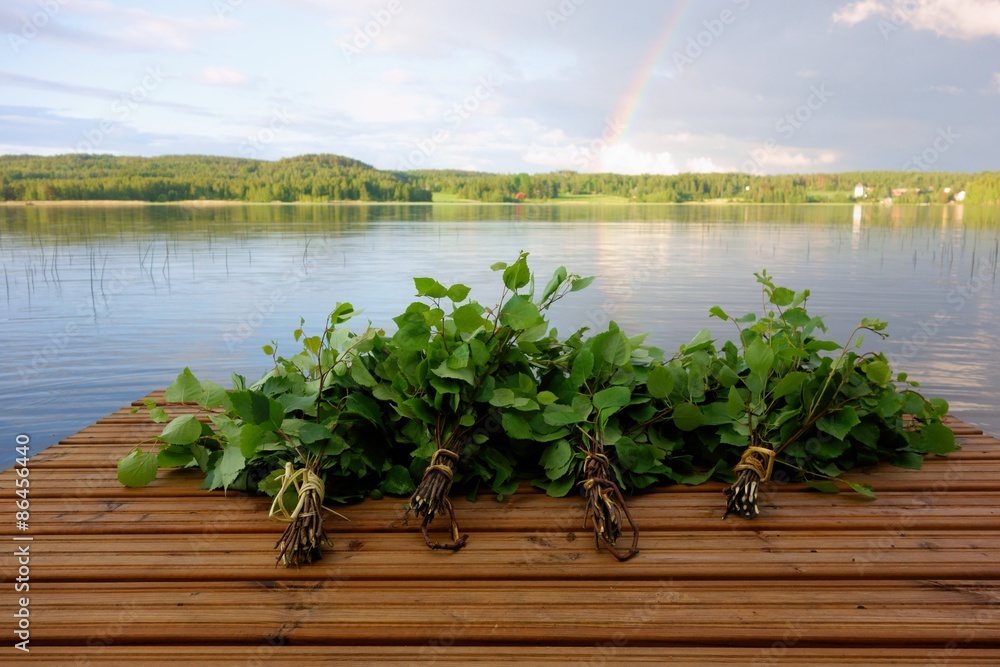 Fototapeta premium Tradycyjne fińskie trzepaczki kąpielowe wykonane ze świeżych liści brzozy i gałązek na mokrym pomostu nad jeziorem podczas Nocy Świętojańskiej.