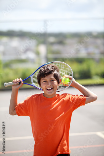 Young boy outside in sun with tennis racquet and ball - portrait format with copy space above