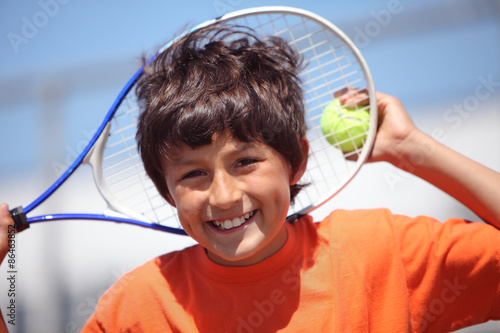 Young boy outside in sun with tennis racquet and ball - portrait format with copy space above