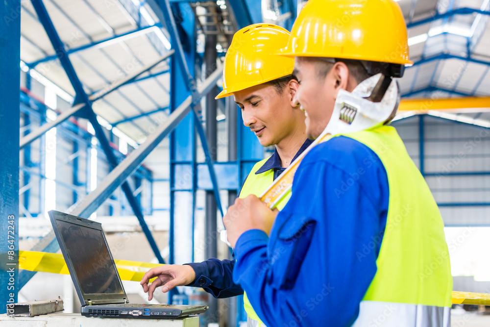 Worker in production plant with laptop Worker in production plant with laptop