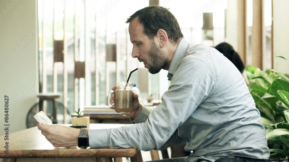 Young man reading newspaper and drinking cocktail in cafe
