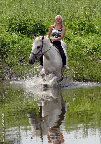 Woman riding horse by rural lake © horsemen