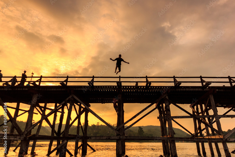 The silhouette young boy jumping of old wooden bridge Bridge collapse Bridge across the river at sangklaburi, kanchanaburi