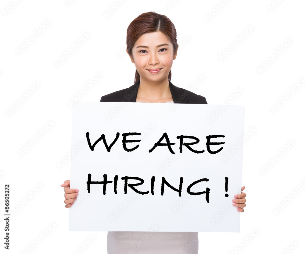 Young businesswoman holding a placard showing with we are hiring Young businesswoman holding a placard showing with we are hiring