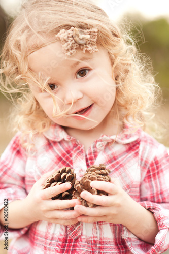 Cute baby girl 2-3 year old holding pine cones outdoors. Looking at camera. Childhood. Playful.