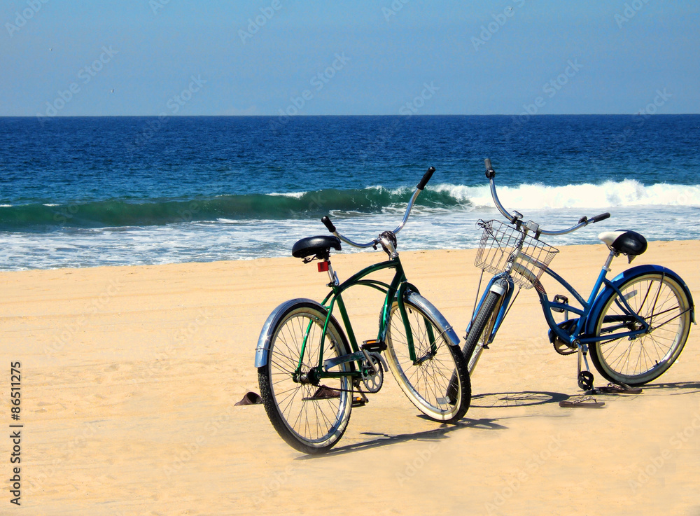 Two bicycles are parked on a beach near the ocean