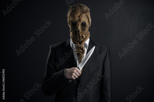 Fear and Halloween theme: a brutal killer in a mask holding a knife on a dark background in the studio