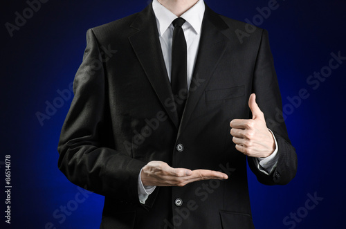 Businessman and gesture topic: a man in a black suit and white shirt showing gestures with hands on a dark blue background in studio isolated